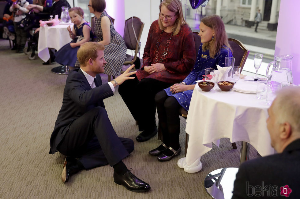 El Príncipe Harry sentado en el suelo hablando con una mujer y una niña en un acto oficial