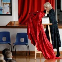 Camilla Parker tratando de retirar una tela que cubre una placa en su visita a la Escuela Roundhill de Bath