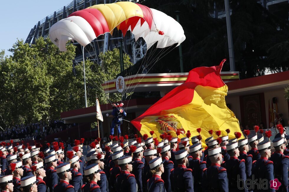 El paracaidista Óscar García aterriza ante la tribuna real con la bandera de España en el desfile militar por la Fiesta Nacional 2022