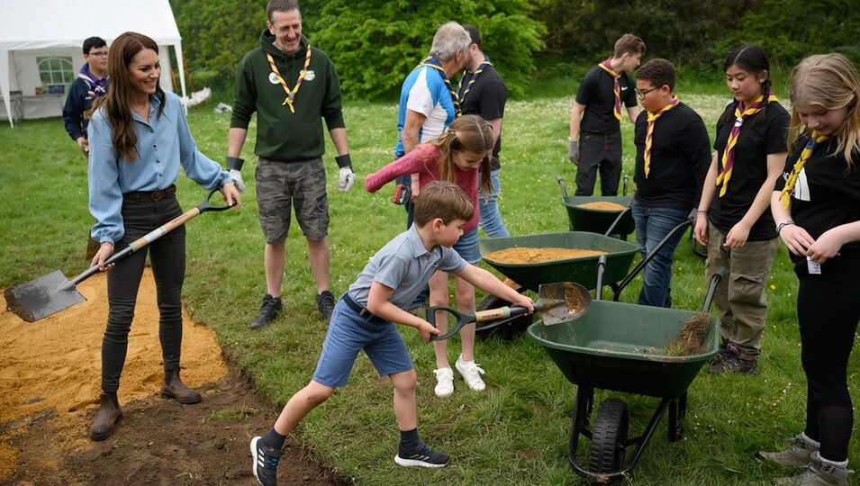 El Príncipe Louis echando tierra en una carretilla en presencia de Kate Middleton y la Princesa Charlotte en the Big Help Out por la Coronación