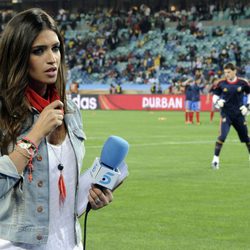 Sara Carbonero a pie de campo con Iker Casillas entrenando detrás