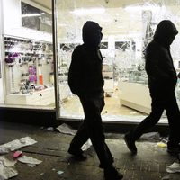 Dos jóvenes caminan junto a una tienda saqueada en los disturbios de Londres