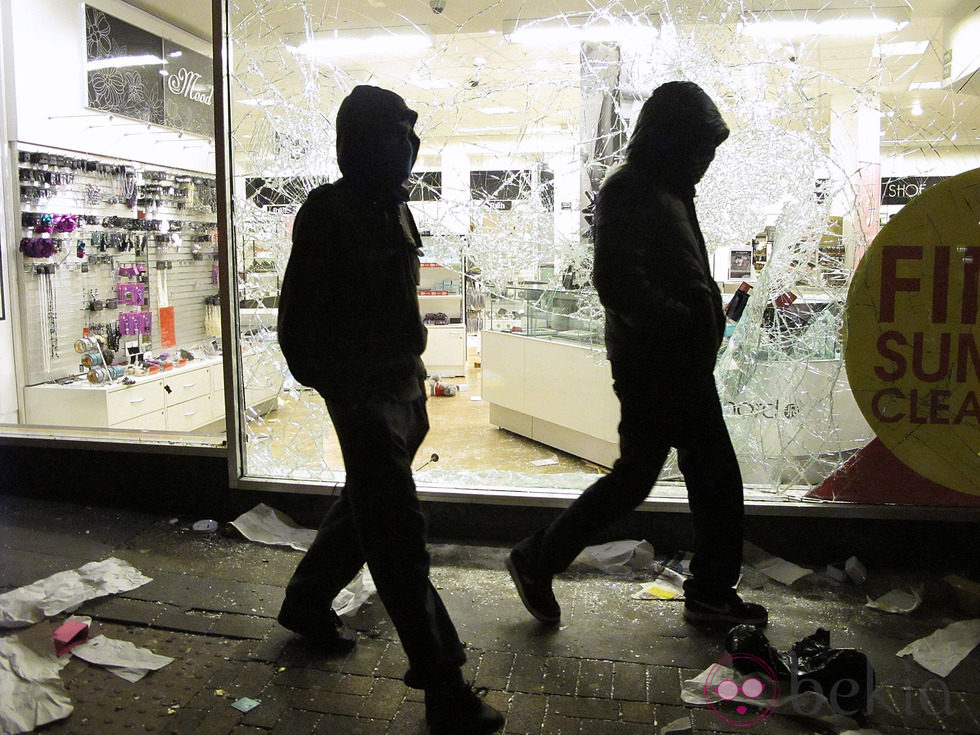 Dos jóvenes caminan junto a una tienda saqueada en los disturbios de Londres