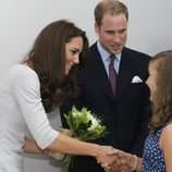 Una niña entrega unas flores a Catalina de Cambridge junto al Príncipe Guillermo en un hospital