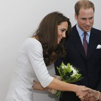 Una niña entrega unas flores a Catalina de Cambridge junto al Príncipe Guillermo en un hospital